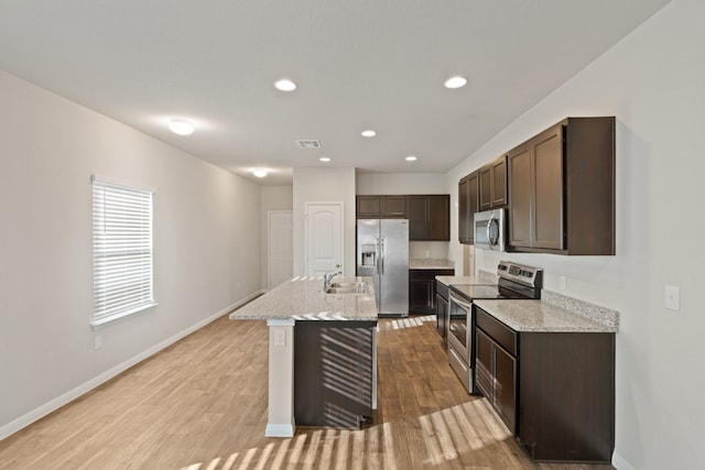 kitchen with a center island with sink, sink, light hardwood / wood-style flooring, light stone countertops, and stainless steel appliances