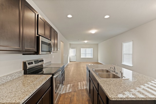 kitchen with dark brown cabinetry, sink, stainless steel appliances, an island with sink, and light wood-type flooring