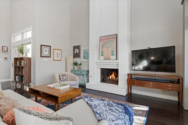 living room with dark hardwood / wood-style flooring, a high ceiling, and a brick fireplace