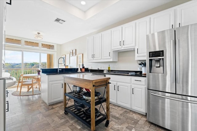 kitchen with a raised ceiling, black gas stovetop, sink, stainless steel fridge, and white cabinetry