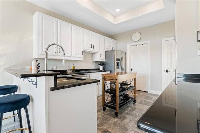 kitchen with a kitchen breakfast bar, a raised ceiling, kitchen peninsula, stainless steel refrigerator with ice dispenser, and white cabinetry