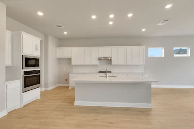 2921 Zuni Path, Leander, TX 78641 - kitchen with oven, under cabinet range hood, black microwave, light wood-type flooring, and a kitchen island with sink