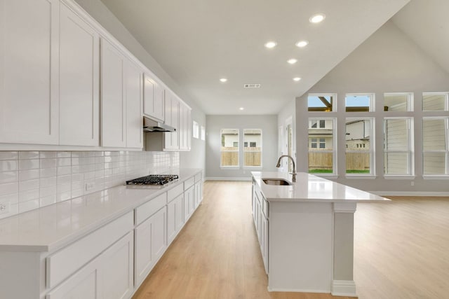 2921 Zuni Path, Leander, TX 78641 - kitchen featuring under cabinet range hood, light wood-style flooring, stainless steel gas cooktop, tasteful backsplash, and recessed lighting