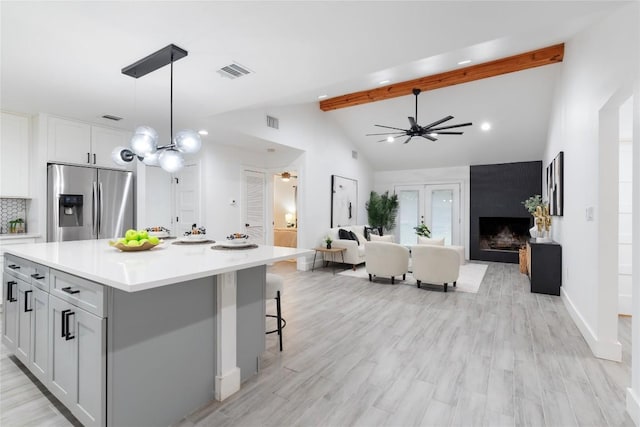 kitchen featuring a large fireplace, hanging light fixtures, stainless steel fridge with ice dispenser, lofted ceiling with beams, and a kitchen island