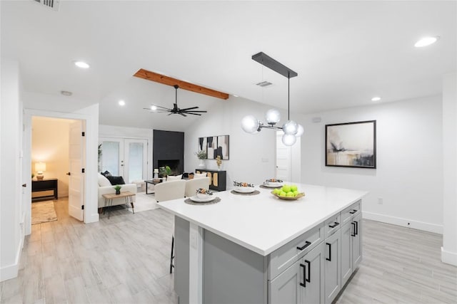 kitchen with light wood-type flooring, ceiling fan, decorative light fixtures, vaulted ceiling with beams, and a kitchen island