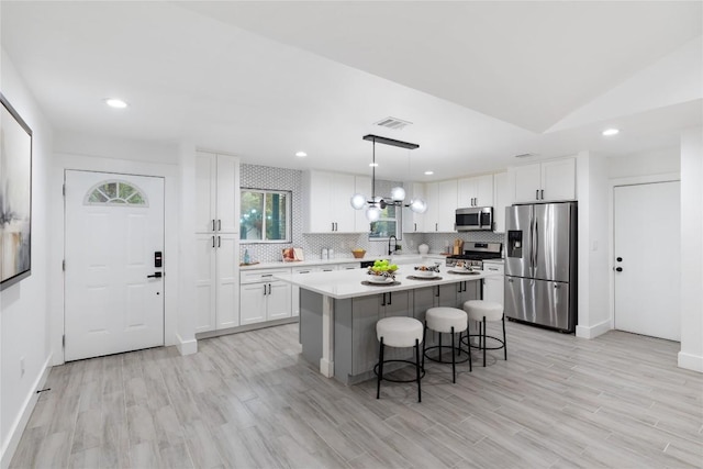 kitchen with appliances with stainless steel finishes, decorative light fixtures, light hardwood / wood-style flooring, a center island, and white cabinetry