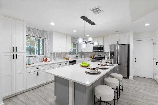 kitchen with white cabinets, light wood-type flooring, appliances with stainless steel finishes, tasteful backsplash, and a kitchen island