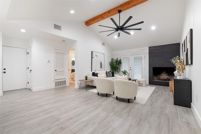 living room featuring beamed ceiling, ceiling fan, a large fireplace, and light hardwood / wood-style flooring