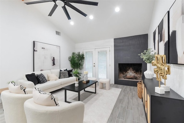 living room featuring high vaulted ceiling, french doors, hardwood / wood-style flooring, ceiling fan, and a fireplace