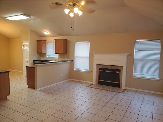 kitchen with a tile fireplace, vaulted ceiling, ceiling fan, light tile patterned floors, and kitchen peninsula