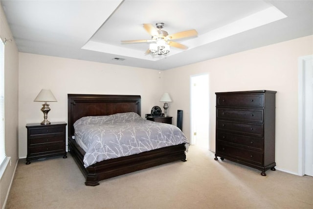 bedroom with a raised ceiling, ceiling fan, and light carpet