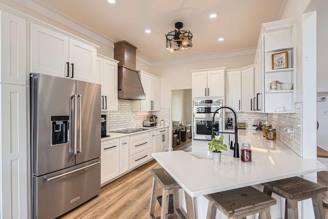 kitchen featuring a kitchen bar, stainless steel appliances, white cabinetry, and wall chimney range hood