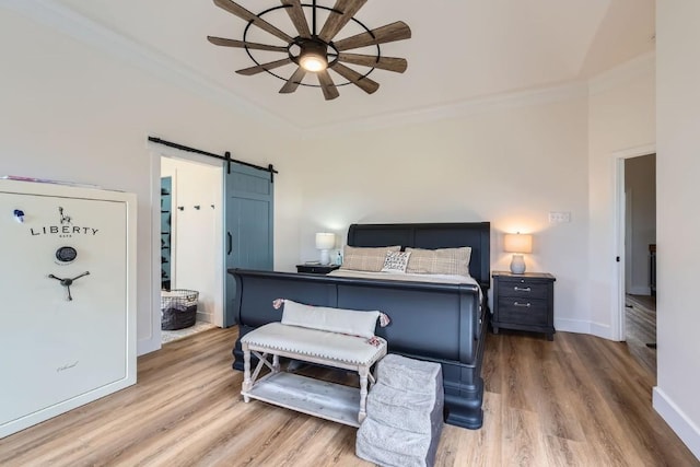 bedroom featuring hardwood / wood-style floors, a barn door, ceiling fan, and ornamental molding