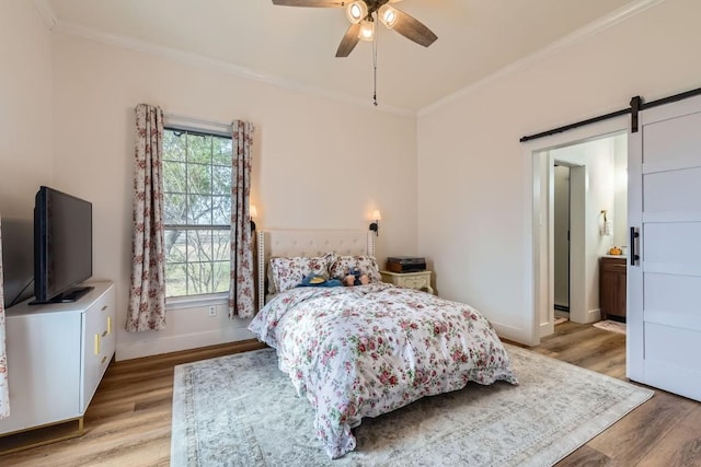 bedroom with ceiling fan, a barn door, light hardwood / wood-style flooring, ensuite bathroom, and ornamental molding