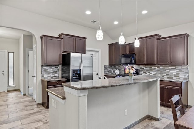 kitchen featuring pendant lighting, backsplash, a kitchen island with sink, stainless steel fridge, and dark brown cabinetry