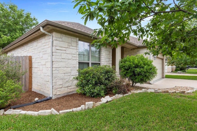 view of side of home with a garage, fence, concrete driveway, and stone siding