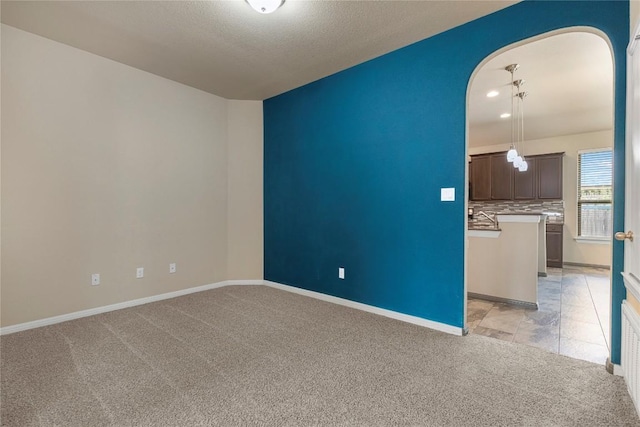 spare room featuring baseboards, arched walkways, a textured ceiling, and light colored carpet