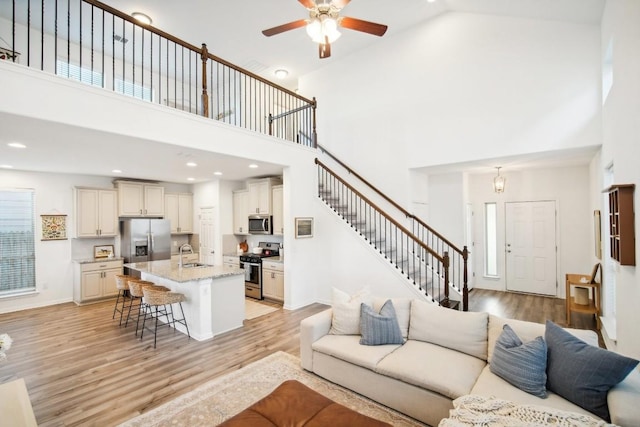 living room with ceiling fan, sink, high vaulted ceiling, and light hardwood / wood-style flooring