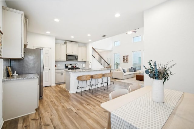 kitchen with a breakfast bar, a center island with sink, sink, light hardwood / wood-style flooring, and appliances with stainless steel finishes