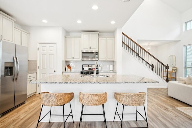 kitchen with sink, light hardwood / wood-style flooring, an island with sink, light stone counters, and stainless steel appliances