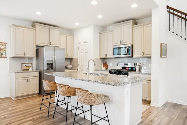 kitchen with a kitchen island with sink, sink, light hardwood / wood-style flooring, light stone counters, and stainless steel appliances