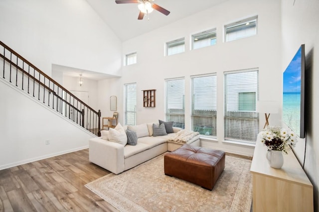 living room featuring ceiling fan, light wood-type flooring, a wealth of natural light, and a towering ceiling