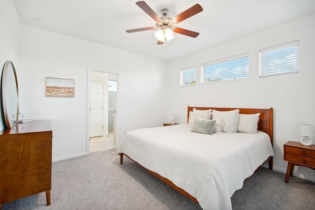 bedroom with ceiling fan, light colored carpet, and ensuite bath