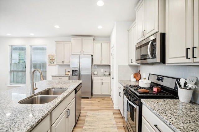 kitchen featuring sink, light stone countertops, appliances with stainless steel finishes, light hardwood / wood-style floors, and white cabinetry