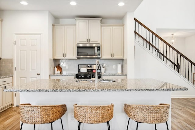 kitchen with stainless steel appliances, light stone counters, light hardwood / wood-style floors, and sink