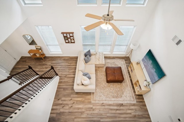 living room featuring hardwood / wood-style floors, ceiling fan, and a towering ceiling