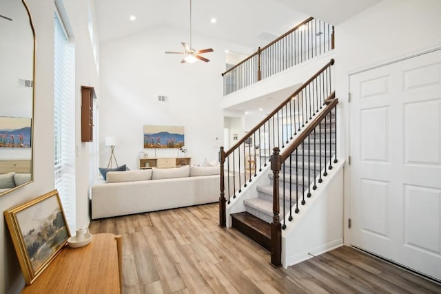 stairs with hardwood / wood-style floors, high vaulted ceiling, and ceiling fan