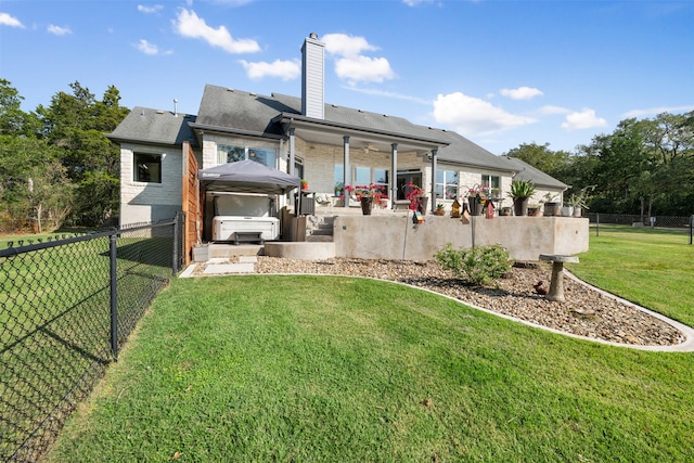 rear view of house featuring a hot tub, a lawn, ceiling fan, and a patio area