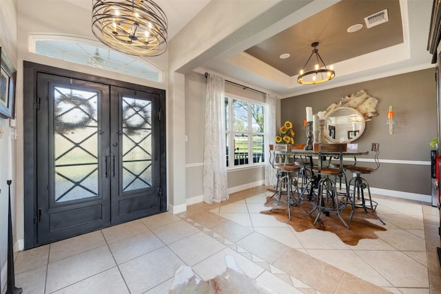 tiled entrance foyer with french doors, ornamental molding, a chandelier, and a tray ceiling