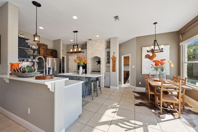 kitchen with light tile patterned flooring, stainless steel fridge with ice dispenser, a kitchen breakfast bar, and decorative light fixtures