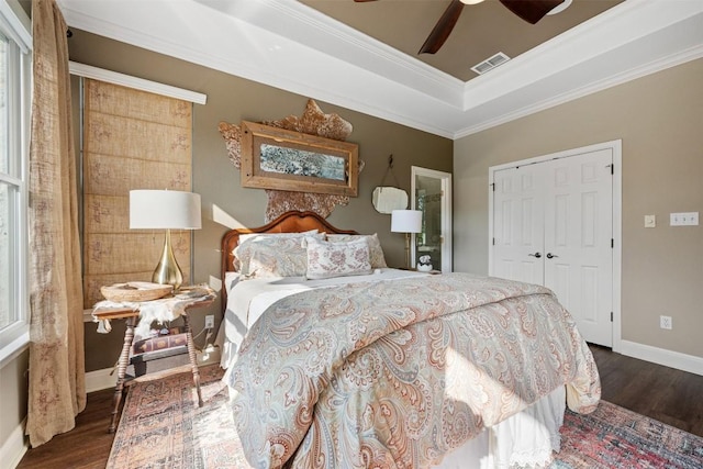 bedroom with dark wood-type flooring, crown molding, a tray ceiling, a closet, and ceiling fan