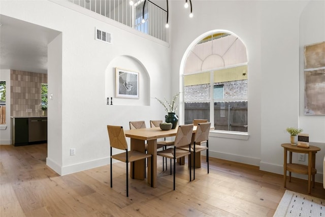 dining space featuring a towering ceiling, light wood-type flooring, and a wealth of natural light