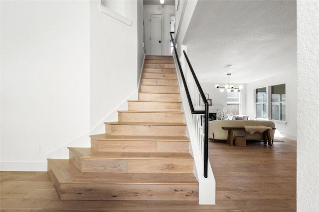 staircase with hardwood / wood-style floors and a notable chandelier