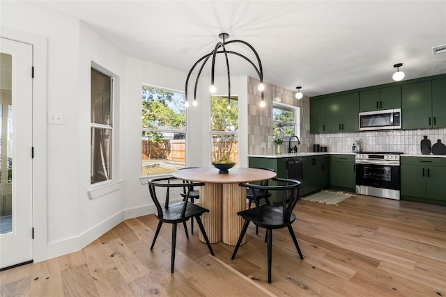 kitchen with green cabinets, light hardwood / wood-style floors, appliances with stainless steel finishes, and tasteful backsplash