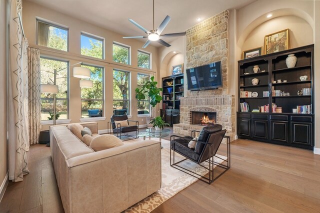 living room featuring ceiling fan, built in features, light hardwood / wood-style floors, and a stone fireplace