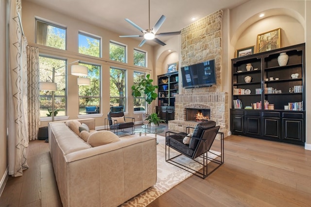 living room with a high ceiling, ceiling fan, a stone fireplace, wood finished floors, and baseboards