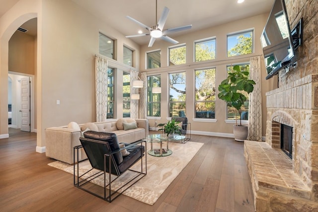 living area featuring arched walkways, a healthy amount of sunlight, wood-type flooring, and a brick fireplace