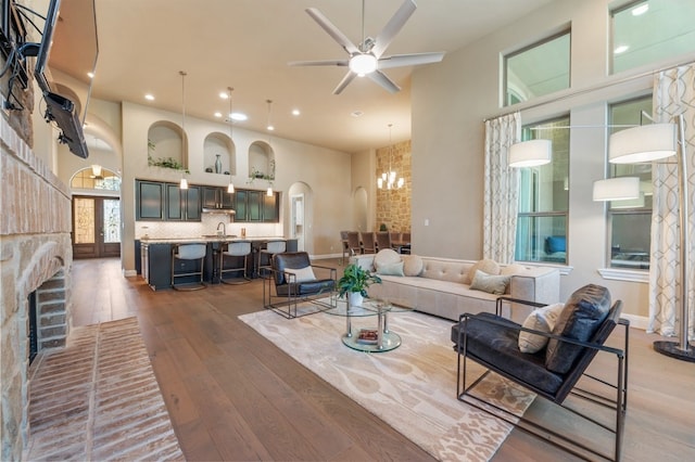 living room with ceiling fan with notable chandelier, dark hardwood / wood-style floors, a brick fireplace, and a towering ceiling