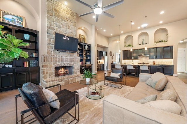 living room with ceiling fan, light wood-type flooring, built in features, and a stone fireplace