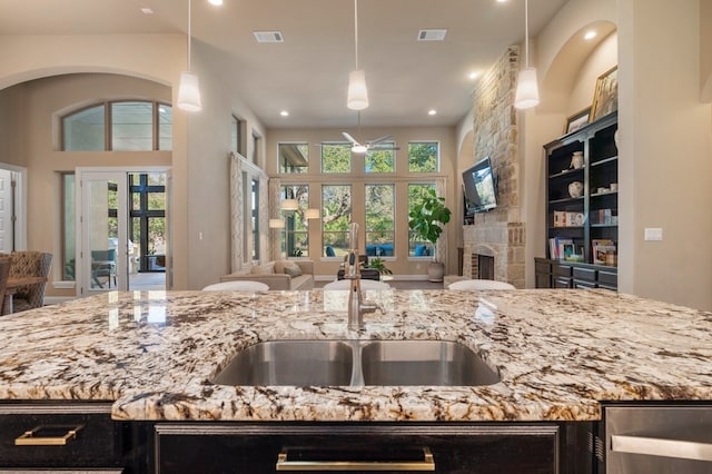 kitchen with french doors, a fireplace, sink, hanging light fixtures, and light stone counters