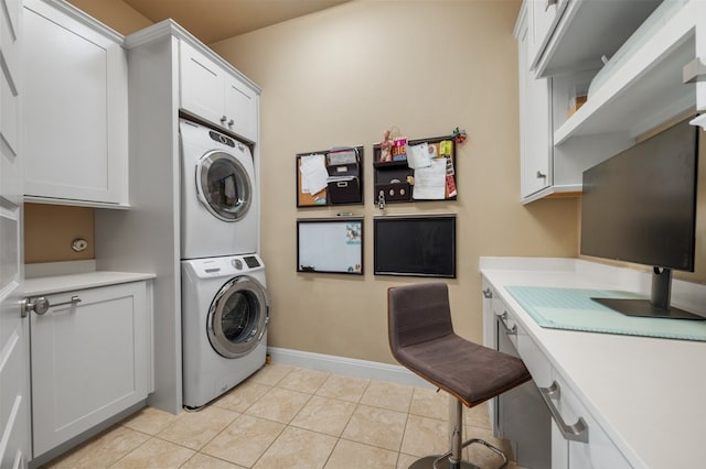 laundry area with stacked washer / drying machine, light tile patterned floors, and cabinets