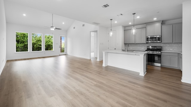 kitchen with stainless steel appliances, gray cabinets, open floor plan, backsplash, and light countertops