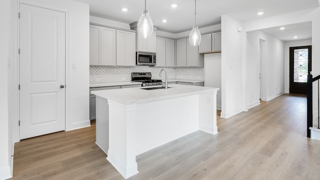 kitchen featuring appliances with stainless steel finishes, gray cabinetry, a sink, an island with sink, and light wood-type flooring