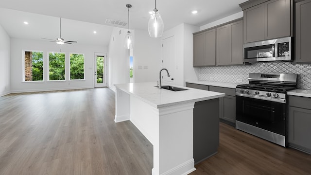 kitchen with appliances with stainless steel finishes, a sink, gray cabinetry, open floor plan, and decorative backsplash