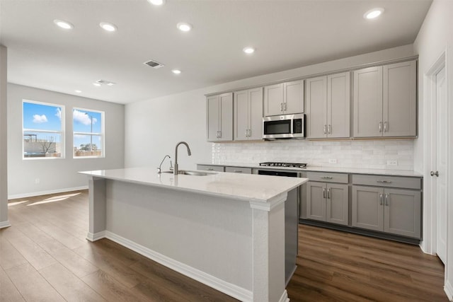 kitchen with a kitchen island with sink, appliances with stainless steel finishes, a sink, and gray cabinetry