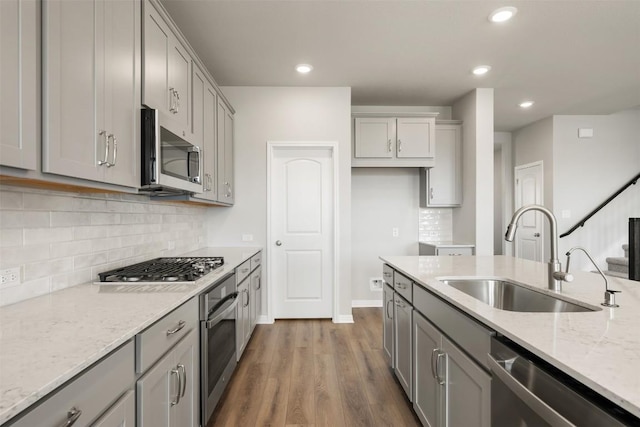 kitchen featuring light stone counters, gray cabinetry, dark wood-type flooring, a sink, and appliances with stainless steel finishes